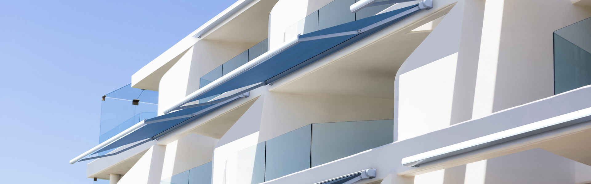 Closeup modern white apartment building with glass balcony against blue sky, full frame horizontal composition with copy space